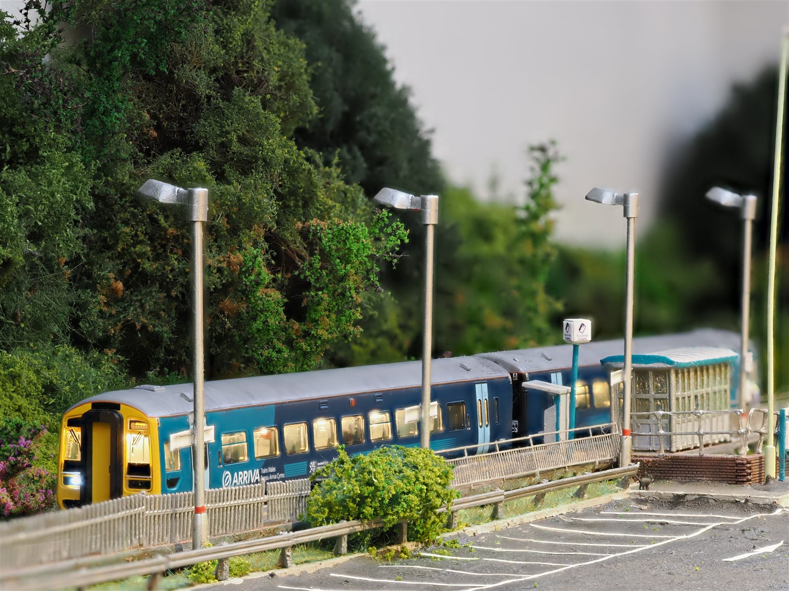 Arriva Trains Wales unit with illuminated headlights under platform lamps