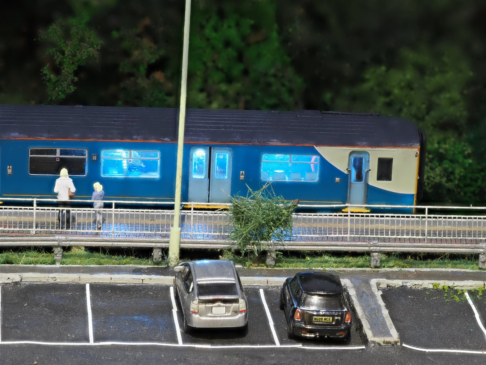 Passengers on the platform at night with parked cars in the foreground