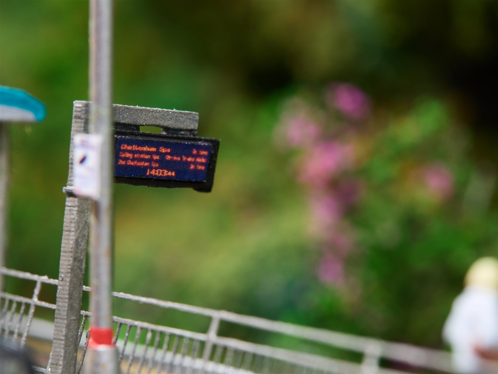 Close-up of the miniature scale platform PID detail on Maesteg showing 14:03:44 and Cheltenham Spa train